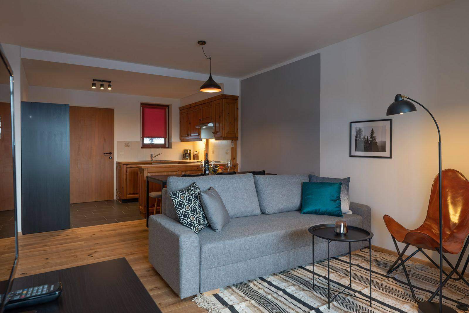 Bright living room with sofa, leather armchair and kitchen – holiday apartment on the Gerlitzen Alpe